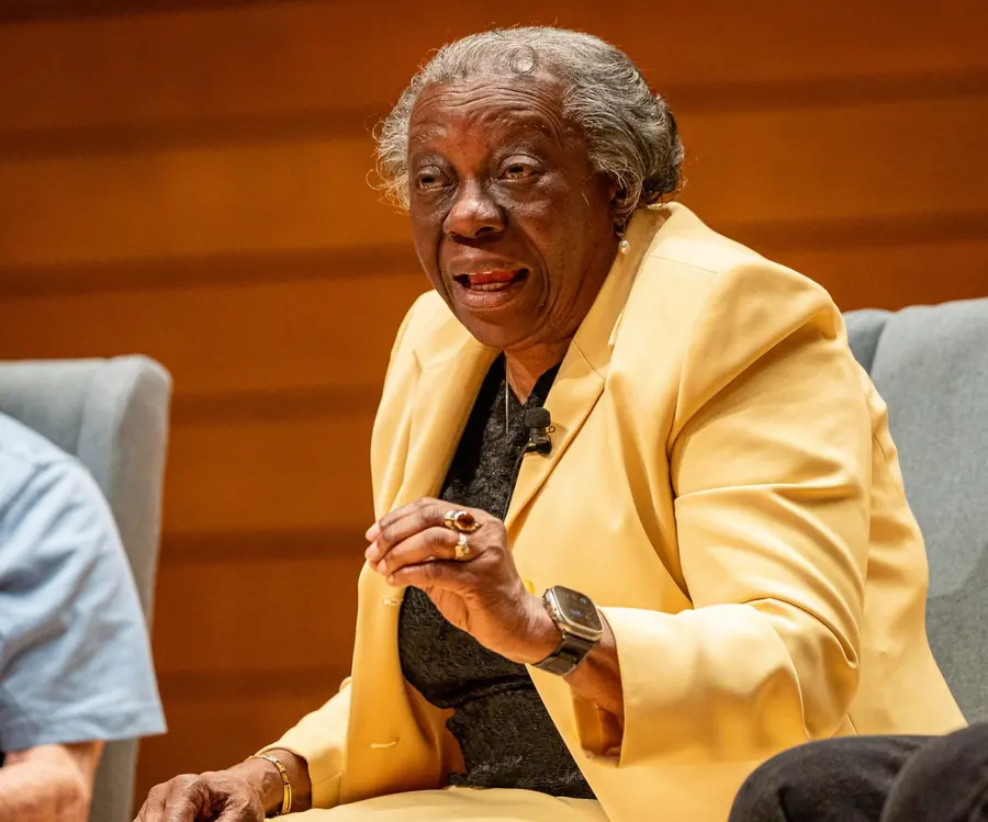 A panelist in a yellow blazer speaking with her hands raised